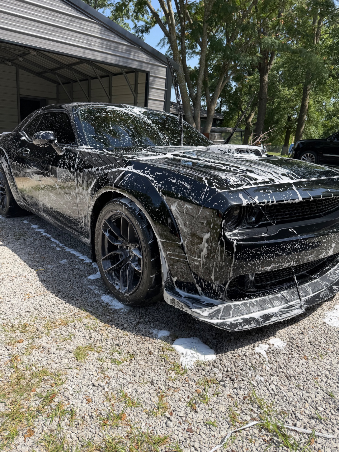 Black Dodge Challenger Hellcat covered in snow foam during a wash